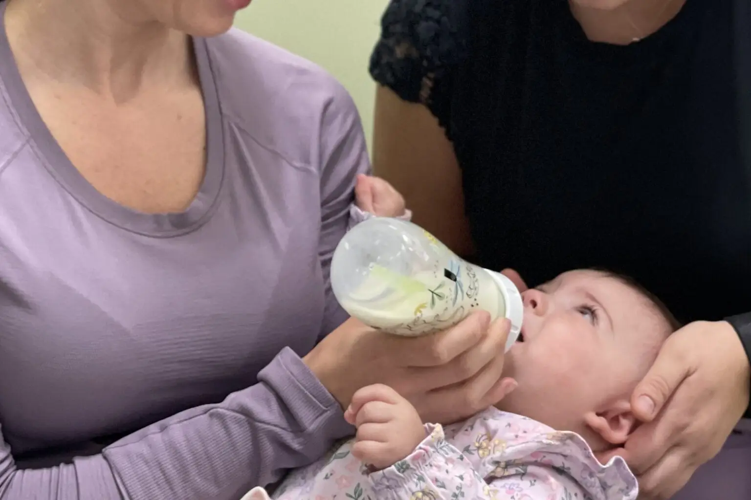 Baby taking a bottle while a chiropractor checks jaw and neck tension