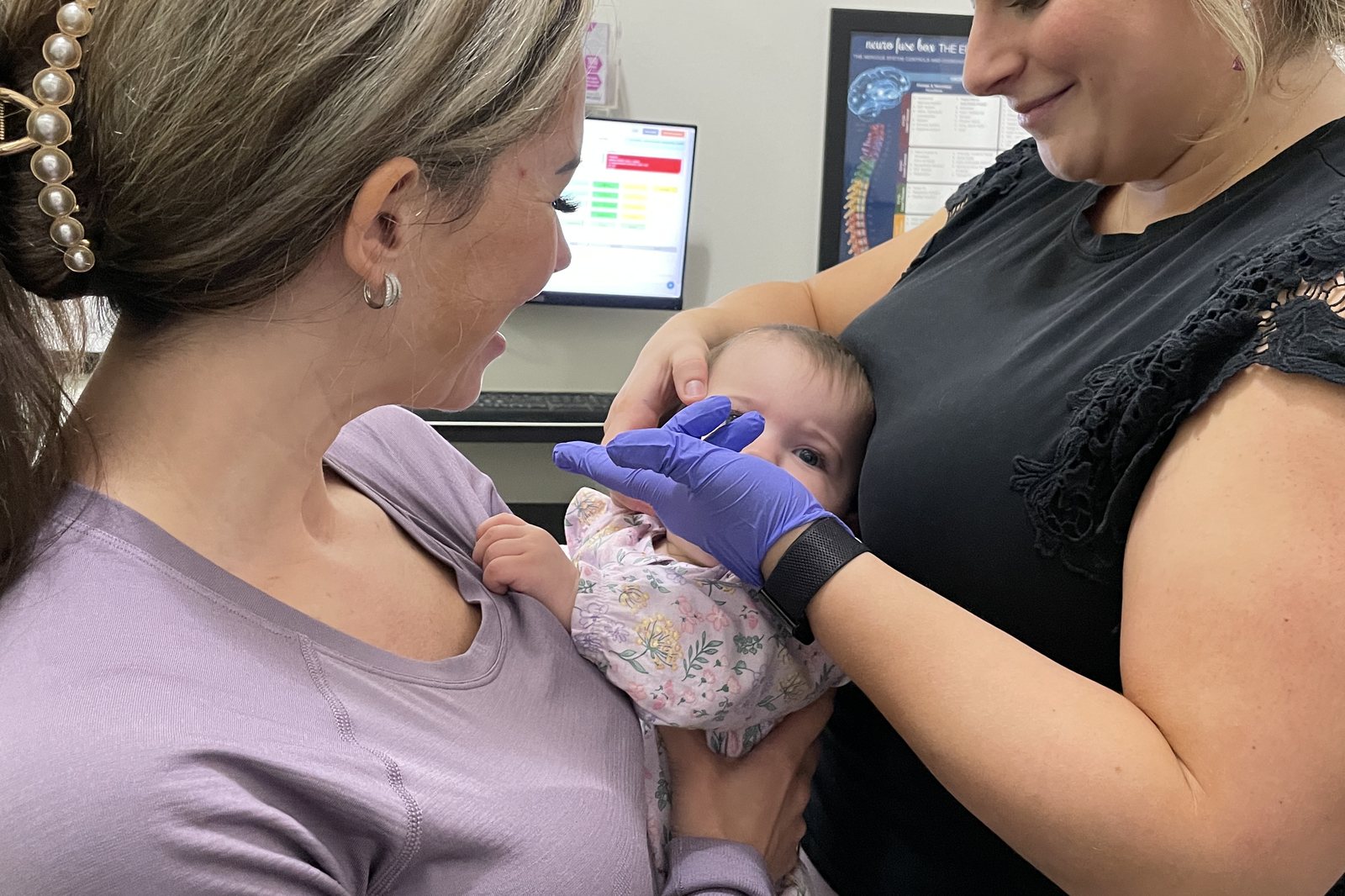 Gloved hand working gently along a baby jaw while a parent holds the baby