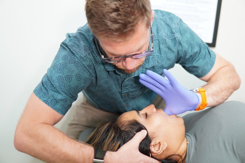 A chiropractor working gently along a patient jaw and upper neck