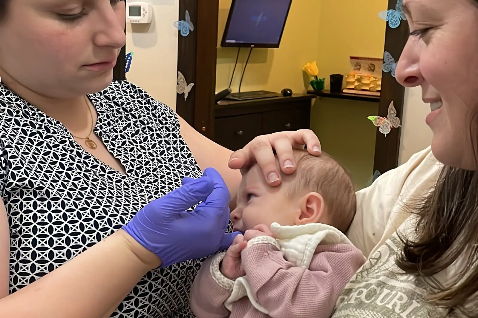 Gentle hands resting on a baby head during a cranial check while a parent holds the baby