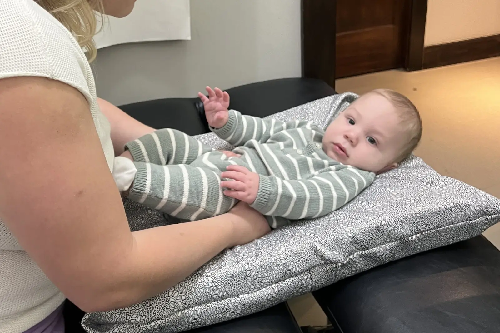 Relaxed baby lying on a padded adjusting table with a parent nearby
